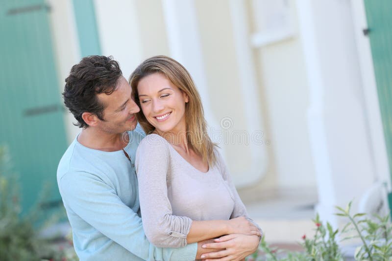 Loving middle-aged couple embracing in front their new home