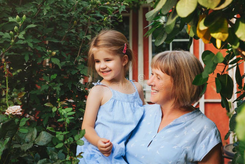 Loving Middle Aged Grandma Holding Smiling Cute Girl Granddaughter While Standing In Garden