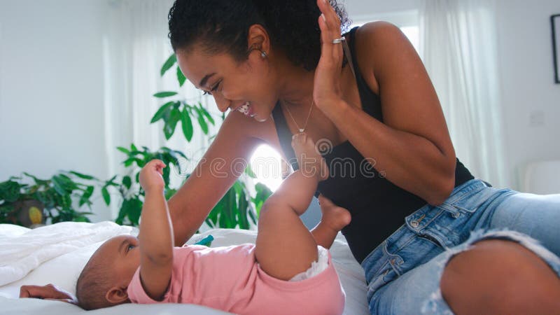 Loving mor som spelar Peekaboo-spel med babydotter som leker på sängen hemma royaltyfria bilder