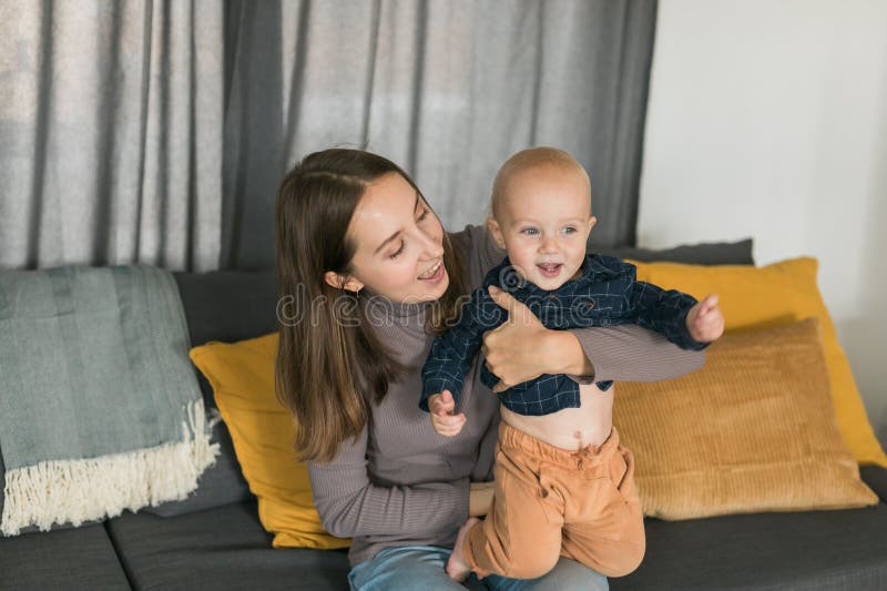 Loving mother holding her cute little baby on lap while sitting in sofa in home