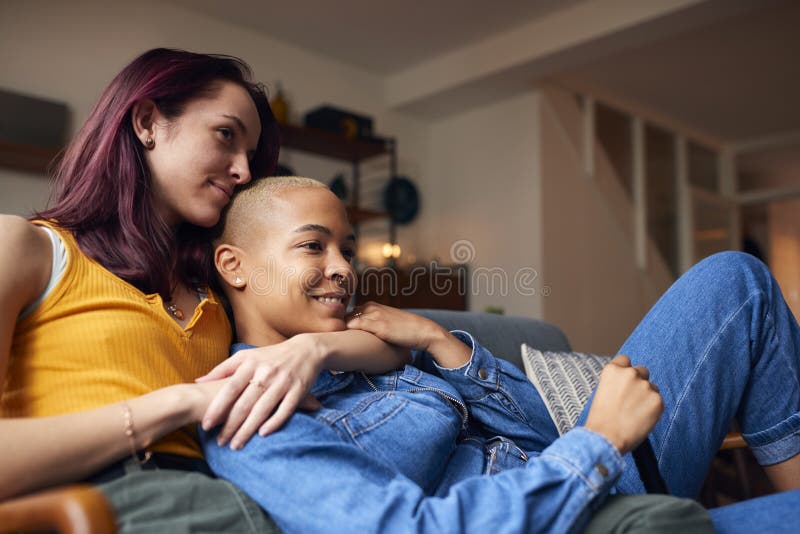 Loving Same Sex Female Couple Lying on Sofa at Home Watching TV and Relaxing Together Stock Image