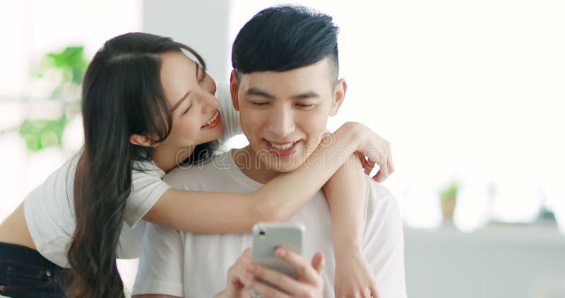 Loving young couple using mobile phone and kissing on sofa at home