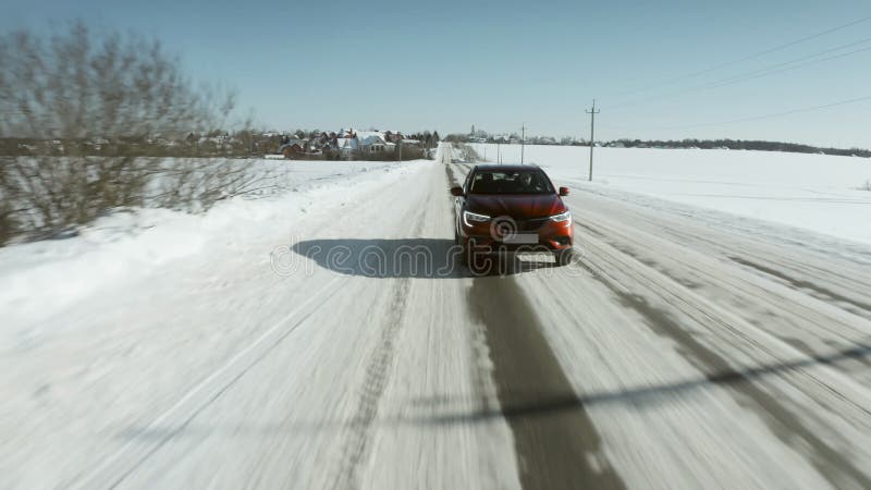 Low altitude aerial shot of a red car or SUV driving along rural snowy road in winter