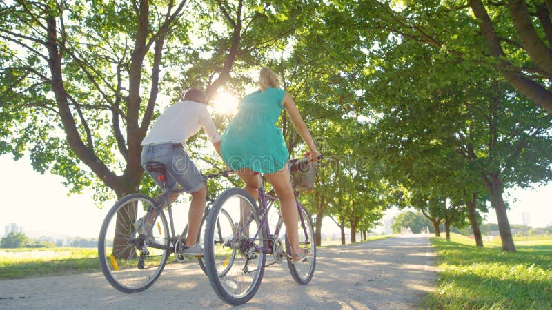 LOW ANGLE: Couple enjoys an active date by riding bikes down a sunlit avenue royalty free stock images