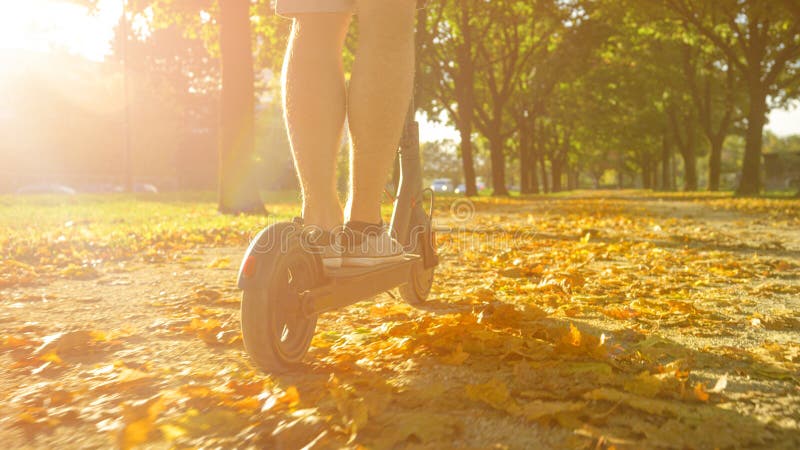 CLOSE UP: Unrecognizable man rides an electric scooter down a scenic gravel path stock image