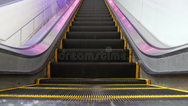 Low angle looped perspective view of modern escalator stairs. Automated elevator mechanism. Yellow line on stairway illuminated