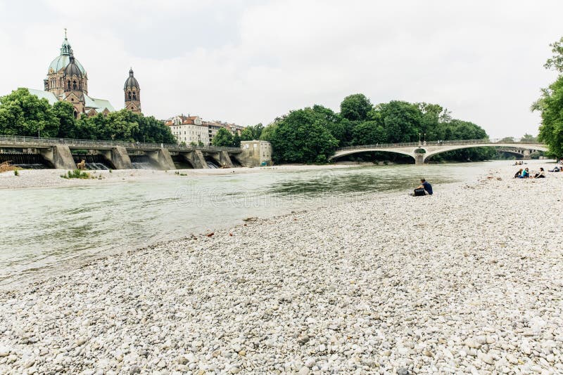 Low angle shot of a beautiful beach with a bridge surrounded by high buildings and green trees.