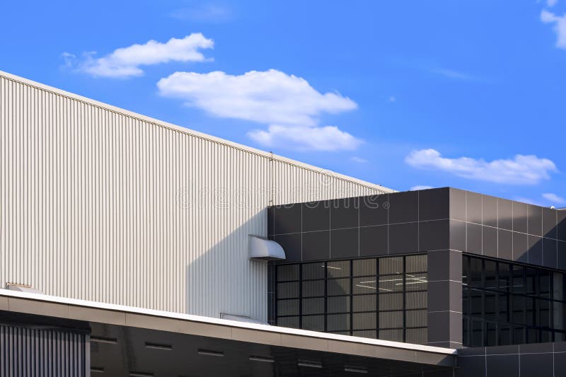 brown office on white corrugated metal industrial building against white clouds in blue sky