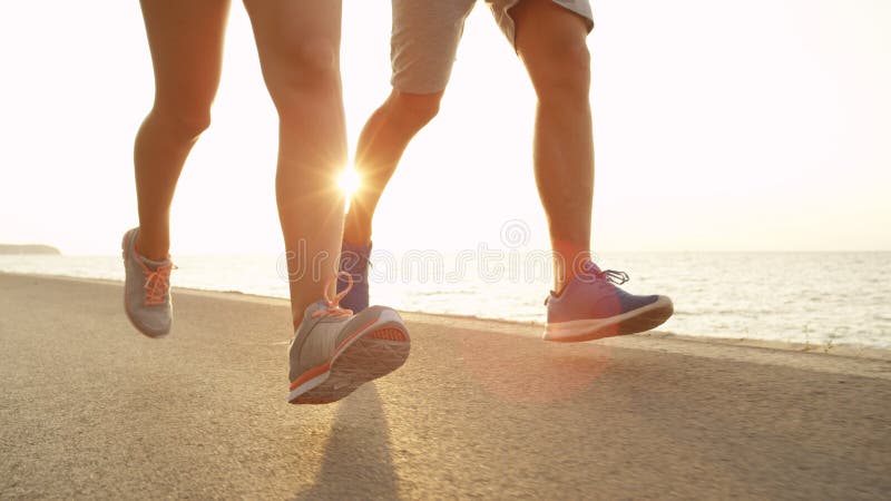 LOW ANGLE, SUN FLARE: Fit couple runs down sunny asphalt ocean road in summer. royalty free stock photo