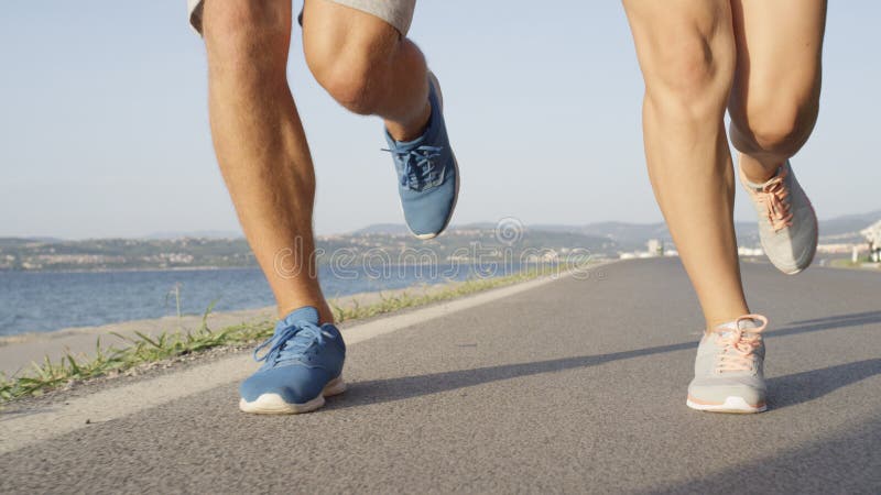 LOW ANGLE: Unrecognizable couple jogs down peaceful walkway near the ocean. stock image