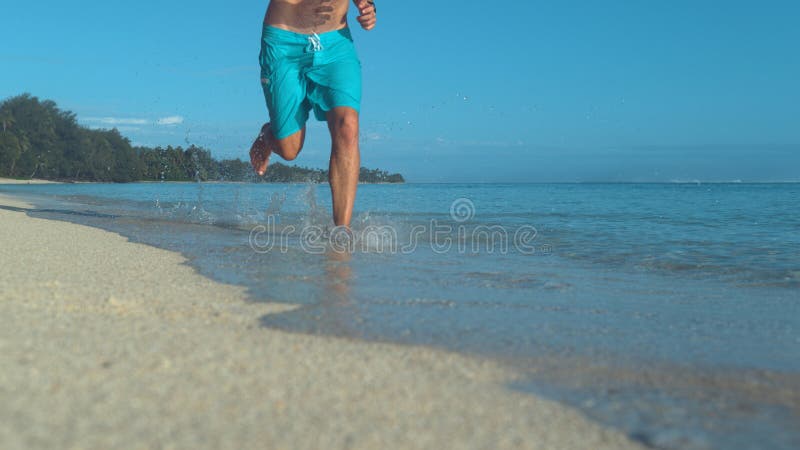 LOW ANGLE: Unrecognizable man runs barefoot down beautiful white sand beach. stock image