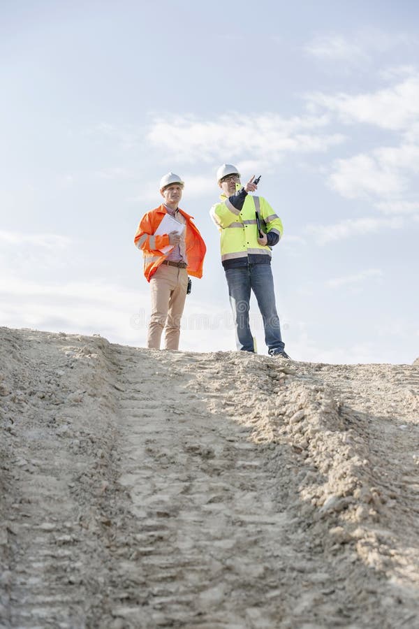 Low angle view of architect showing something to colleague at construction site against sky royalty free stock photo Low angle view of architect showing something to colleague at construction site against sky royalty free stock photo