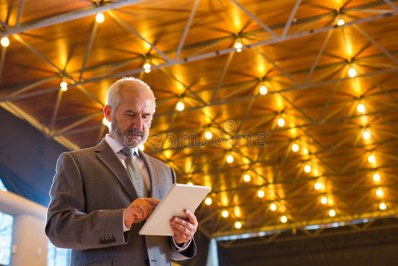 Low angle view of confident senior businessman using digital tablet while standing against illuminated roof stock photo