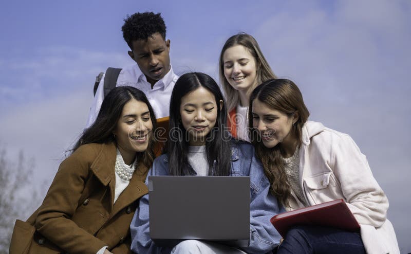 Low angle view of group of diverse university students collaborating on a project using a laptop outdoors stock image