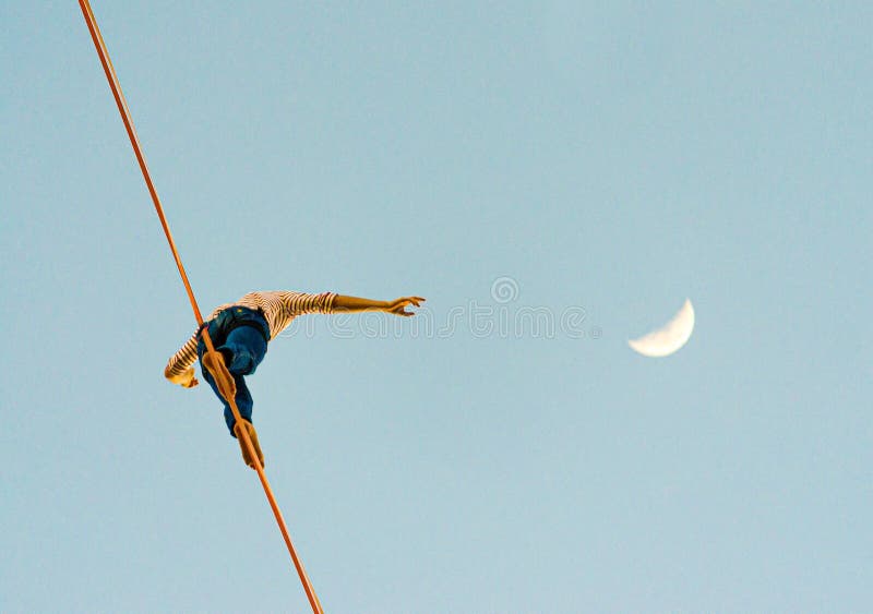 Low angle view of a person walking on a tightrope with the half moon in the blue sky