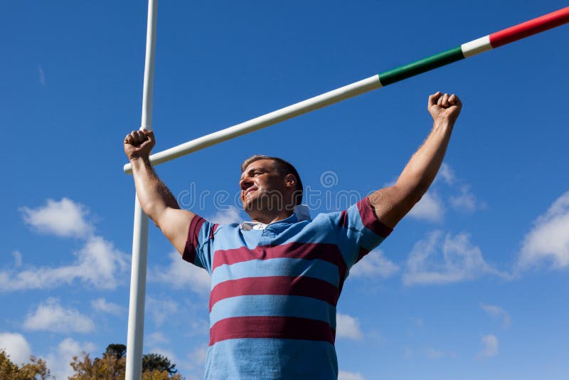 Low Angle View of Smiling Rugby Player with Arms Raised Against Blue