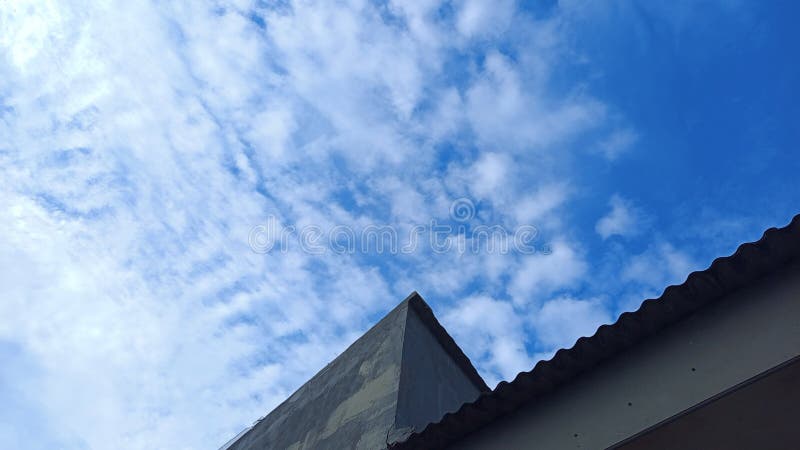 Low-angle view of a triangular rooftop with clear blue sky and scattered clouds, minimalist architecture, natural background