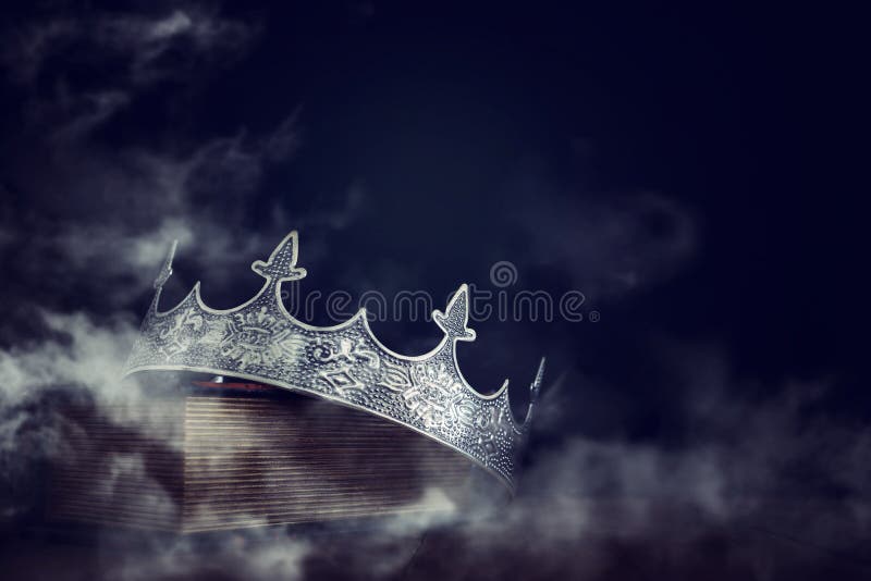 low key image of beautiful queen/king crown over old book and wooden table. vintage filtered. fantasy medieval period. mist and