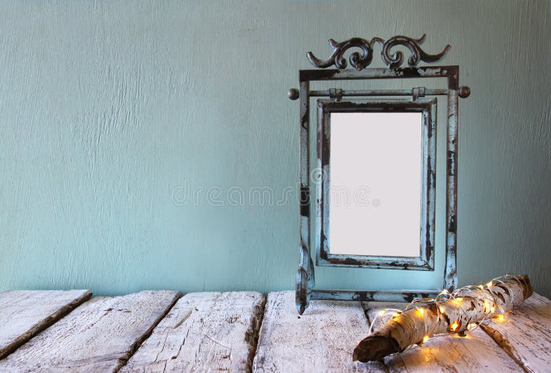 Low key image of old victorian steel blue blank frame next to log tree with fairy christmas lights on wooden table