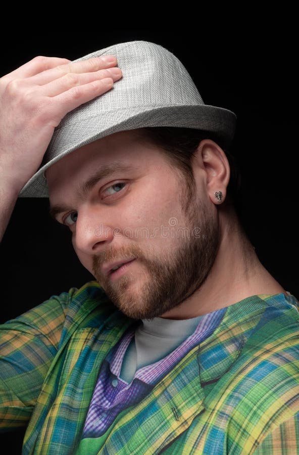 Portrait of good-looking bearded serious man with earring in green trendy blazer putting on stylish grey hat royalty free stock photography Portrait of good-looking bearded serious man with earring in green trendy blazer putting on stylish grey hat royalty free stock photography