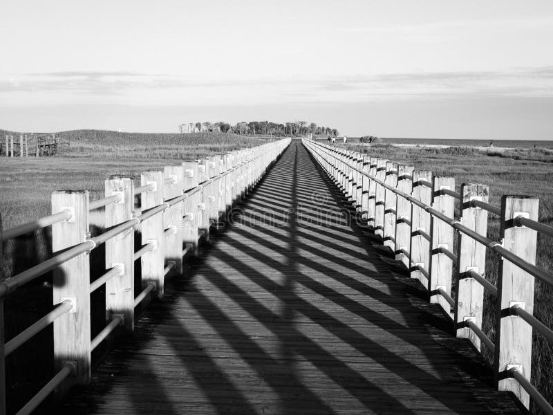 Boardwalk, perspective with vanishing point leading lines and shadow pattern. Low sunlight casts long grid like patterns across a board walk with leading lines royalty free stock photos Boardwalk, perspective with vanishing point leading lines and shadow pattern. Low sunlight casts long grid like patterns across a board walk with leading lines royalty free stock photos