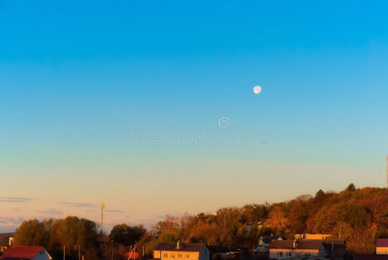 Lua cheia no céu sobre a cidade, alvorecer na vila imagem de stock Lua cheia no céu sobre a cidade, alvorecer na vila imagem de stock