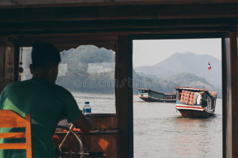 Luang Prabang, Laos - maggio 2019: vista sopra le barche lente di legno laotiane sul Mekong attraverso la finestra di cabina di p fotografia stock libera da diritti