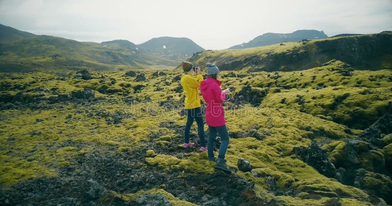 Luchtmening van twee toeristenvrouw het lopen op lavagebieden in IJsland en het maken van foto's De meisjes gebruiken smartphone