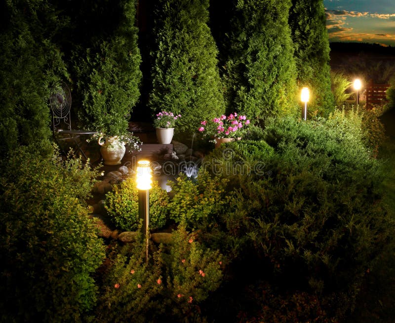 Illuminated home garden patio, plants and fountain on evening dusk. Illuminated home garden patio, plants and fountain on evening dusk