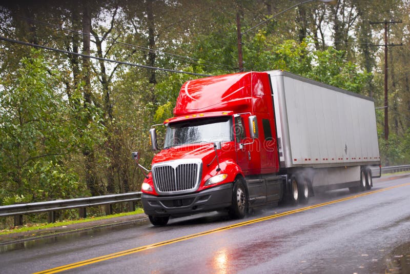 Lucido rosso moderno in rimorchio del camion dei semi della pioggia sulla pioggia della strada immagine stock