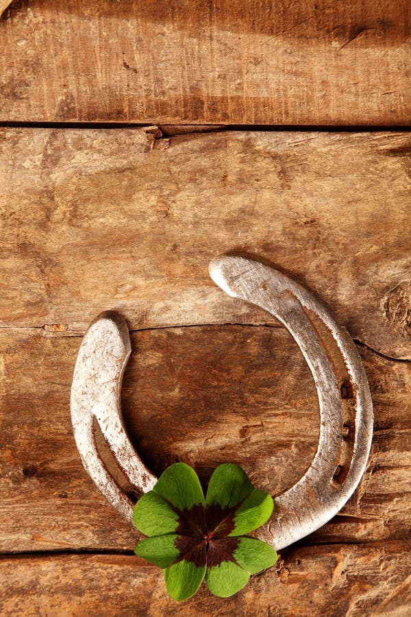 Lucky horseshoe and Irish shamrock or four-leaf clover on a rustic wooden board background with copyspace for your greeting or wishes, overhead view