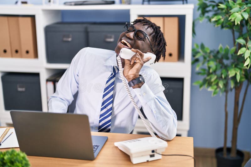 Lucrător american în afaceri din Africa Americană care vorbește la telefon folosind un laptop la birou stock photography