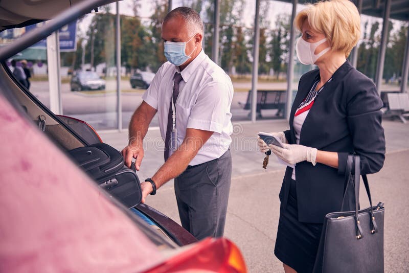 Lucrător de tip aeroport care ajută o femeie de afaceri să pună bagajele în portbagaj stock photography
