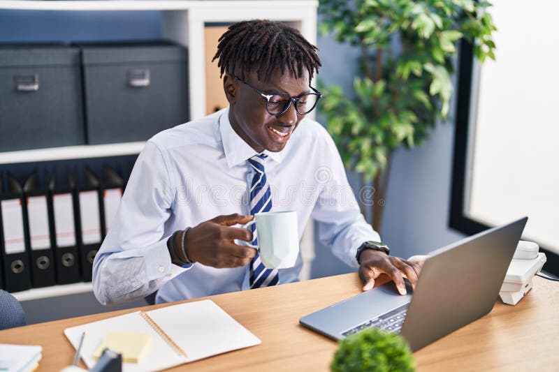 Lucrător din America Africană care utilizează un laptop care bea cafea la birou stock image