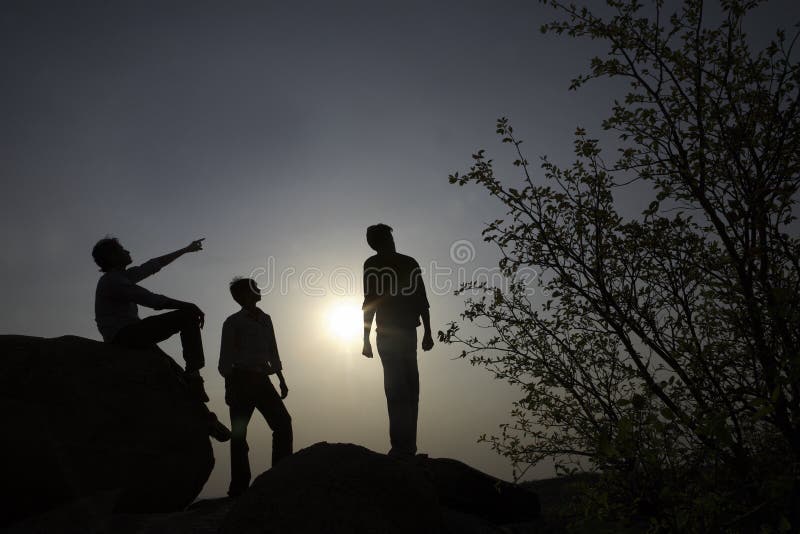 Silhouettes of three people, possibly hikers, resting on rocks on a mountaintop or hilltop. Silhouettes of three people, possibly hikers, resting on rocks on a mountaintop or hilltop.