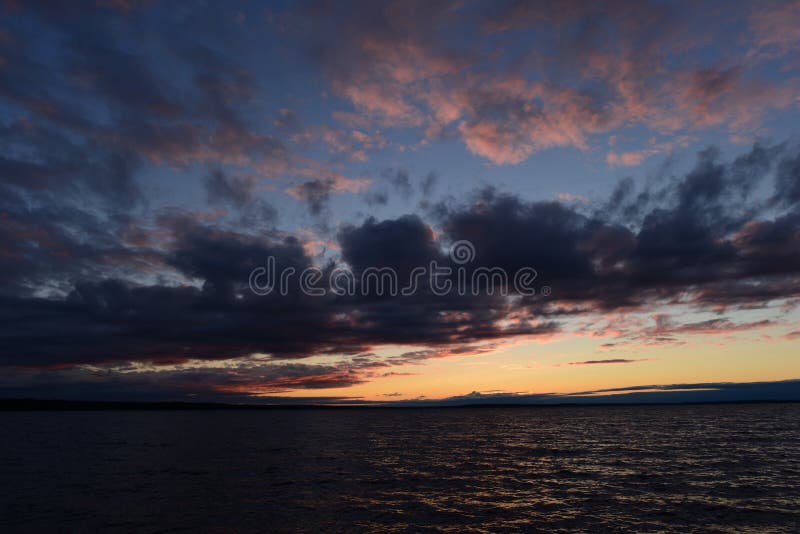 Lueur sombre de tombée de la nuit du ciel en nuages foncés au-dessus des vagues de l'eau du lac photographie stock libre de droits Lueur sombre de tombée de la nuit du ciel en nuages foncés au-dessus des vagues de l'eau du lac photographie stock libre de droits