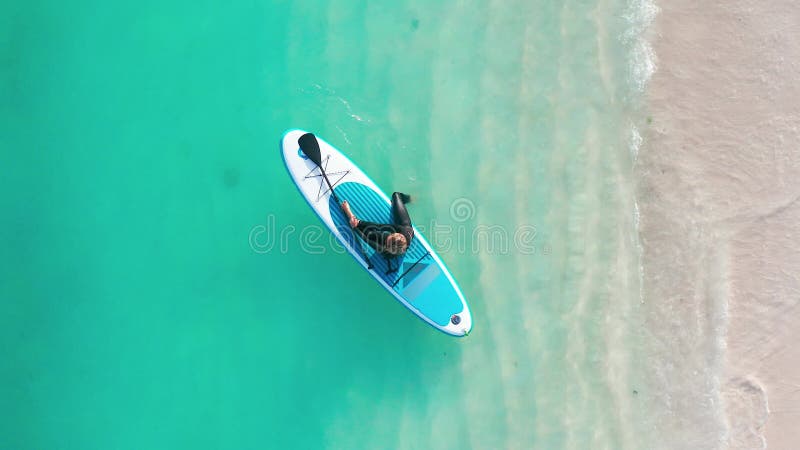 Luftbild einer Frau auf einem Surfbrett im türkisfarbenen Wasser der Malediven. stock footage