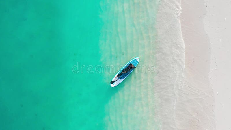 Luftbild einer Frau auf einem Surfbrett im türkisfarbenen Wasser der Malediven. stock video