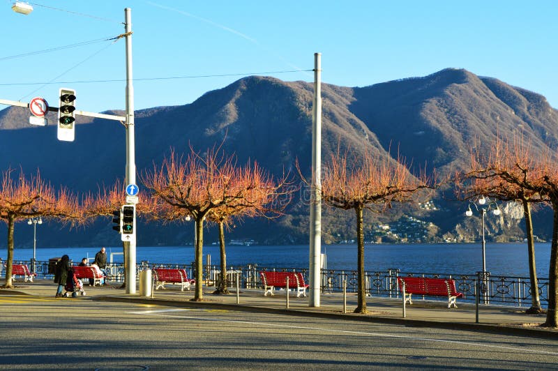 LUGANO SZWAJCARIA, LISTOPAD, - 27, 2017: Zadziwiający spadek zimy widok jezioro przód Lugano z pięknymi drzewami, Szwajcaria fotografia stock LUGANO SZWAJCARIA, LISTOPAD, - 27, 2017: Zadziwiający spadek zimy widok jezioro przód Lugano z pięknymi drzewami, Szwajcaria fotografia stock