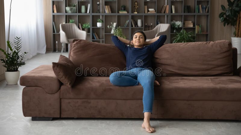 Lugn indian i årtusendet sitter på soffa-händer bakom huvudet arkivbilder