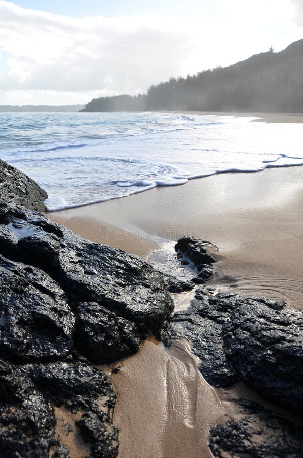 The rocky edges of Lumahai Beach in Kauai, Hawaii. Featured in the movie South Pacific, it's a private beach and unsafe to swim at. Close up of sand and lava rock as the tide rolls in. The rocky edges of Lumahai Beach in Kauai, Hawaii. Featured in the movie South Pacific, it's a private beach and unsafe to swim at. Close up of sand and lava rock as the tide rolls in.