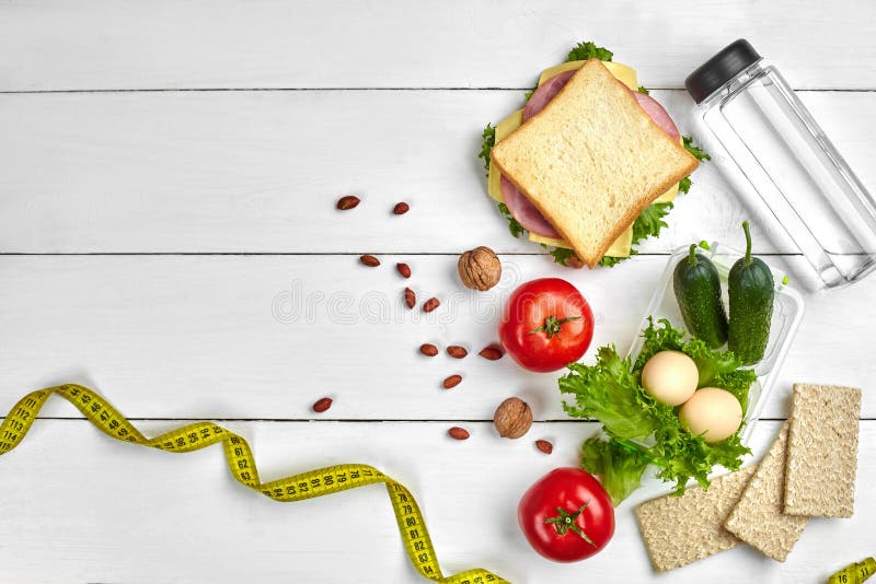 Lunch boxes with sandwich and fresh vegetables, bottle of water, nuts and eggs on white wooden background. Top view with royalty free stock image Lunch boxes with sandwich and fresh vegetables, bottle of water, nuts and eggs on white wooden background. Top view with royalty free stock image