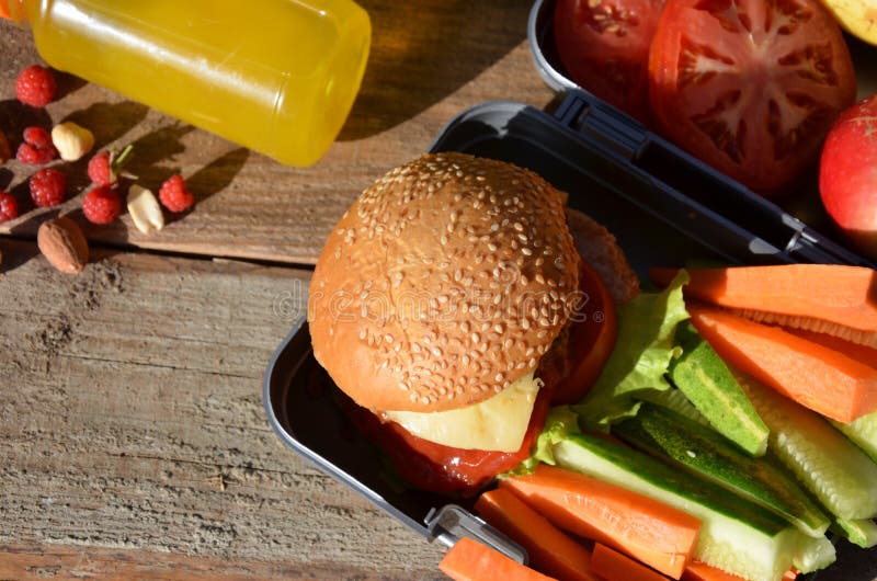 Lunch boxes with food ready to go for work or school, meal preparation or dieting concept. Hamburgers with lettuce. yellow orange juice. with banana nuts. Sliced vegetables carrots and cucumber. Lunch boxes with food ready to go for work or school, meal preparation or dieting concept. Hamburgers with lettuce. yellow orange juice. with banana nuts. Sliced vegetables carrots and cucumber.