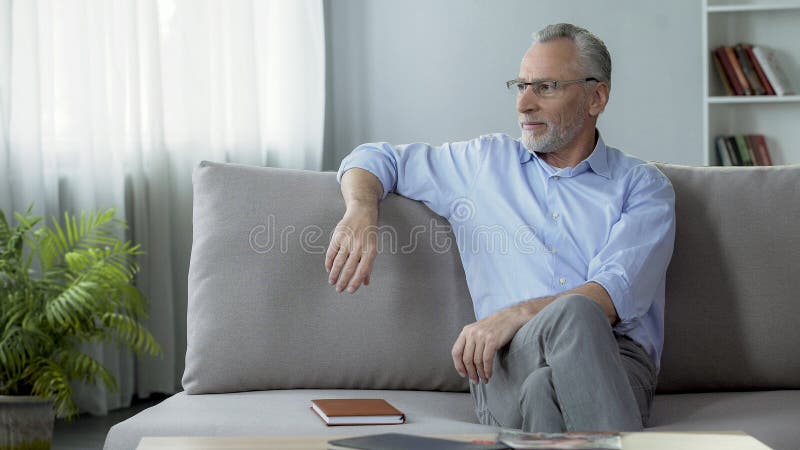 Lunettes de port saines d'homme supérieur, se reposant sur le sofa, rêvant des vacances image stock Lunettes de port saines d'homme supérieur, se reposant sur le sofa, rêvant des vacances image stock