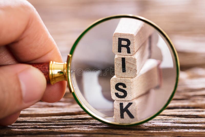 Close-up Of A Person Inspecting Risk Block With Magnifying Glass On Wooden Table. Close-up Of A Person Inspecting Risk Block With Magnifying Glass On Wooden Table