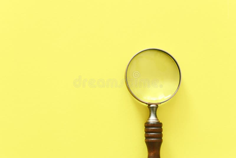 Vintage magnifying glass with wooden handle over yellow background. top view, flat lay. Vintage magnifying glass with wooden handle over yellow background. top view, flat lay.