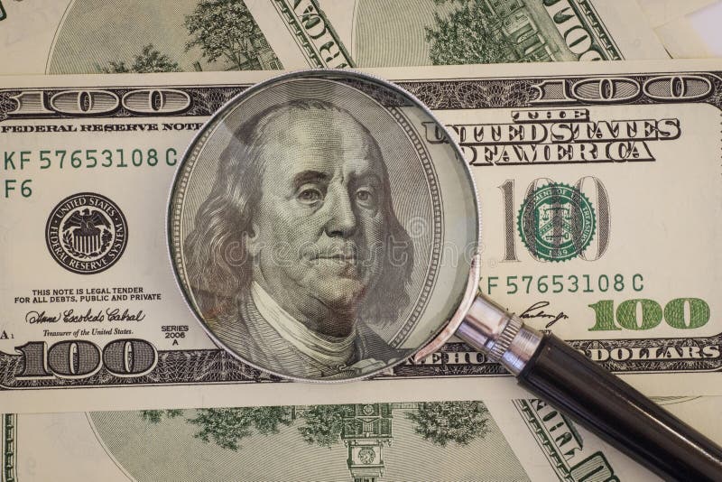 A lupa encontra-se em cem notas de dólar imagem de stock A lupa encontra-se em cem notas de dólar imagem de stock