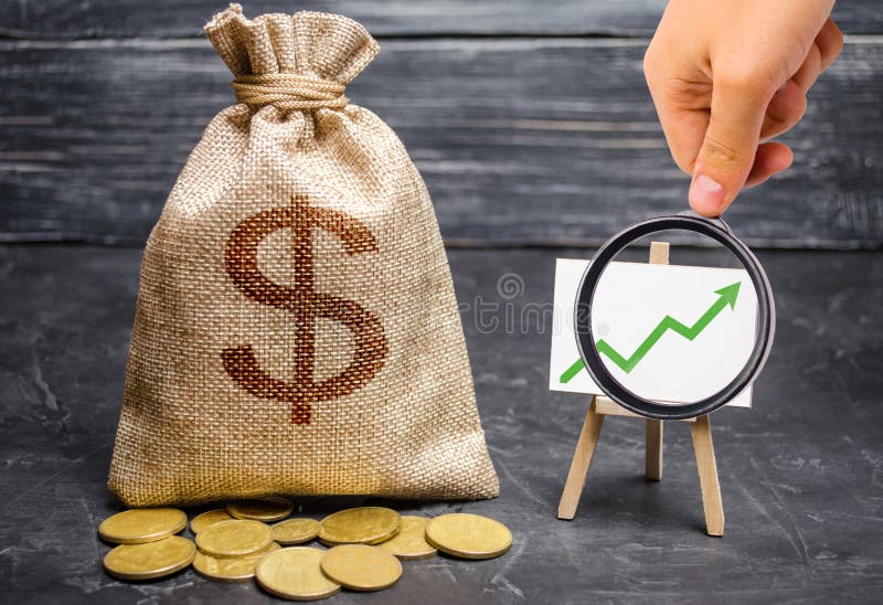 Magnifying glass is looking at the green arrow up on the chart and a Bag with money. concept of increasing profits and revenues, increasing capital and increasing the efficiency of a business. Success. Magnifying glass is looking at the green arrow up on the chart and a Bag with money. concept of increasing profits and revenues, increasing capital and increasing the efficiency of a business. Success