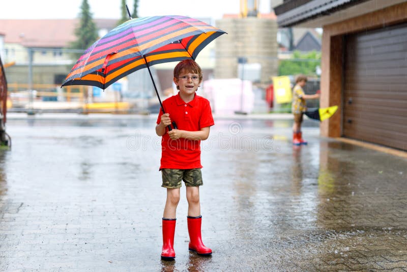 Lura pojken som bär röda regnkängor och går med det färgrika paraplyet på stadsgatan Barn med exponeringsglas på sommardag royaltyfri bild Lura pojken som bär röda regnkängor och går med det färgrika paraplyet på stadsgatan Barn med exponeringsglas på sommardag royaltyfri bild