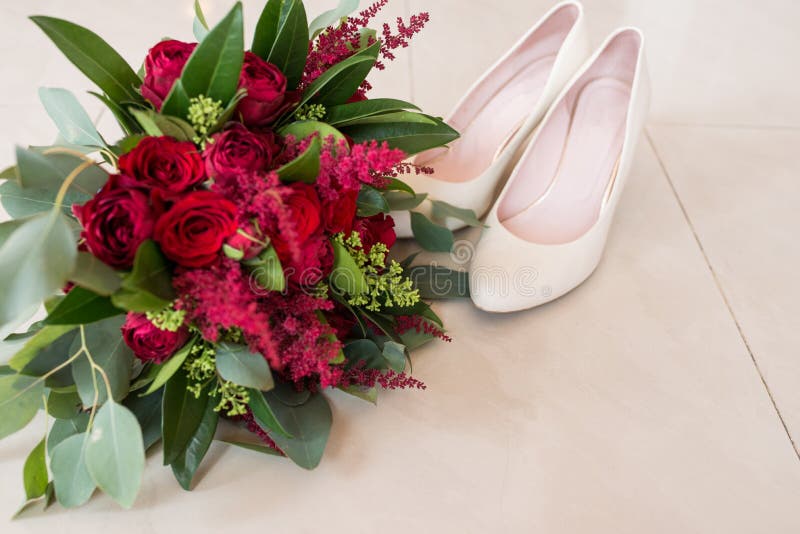 Lush bridal Bouquet of red roses and a lot of greenery with elegant bridal shoes. Wedding